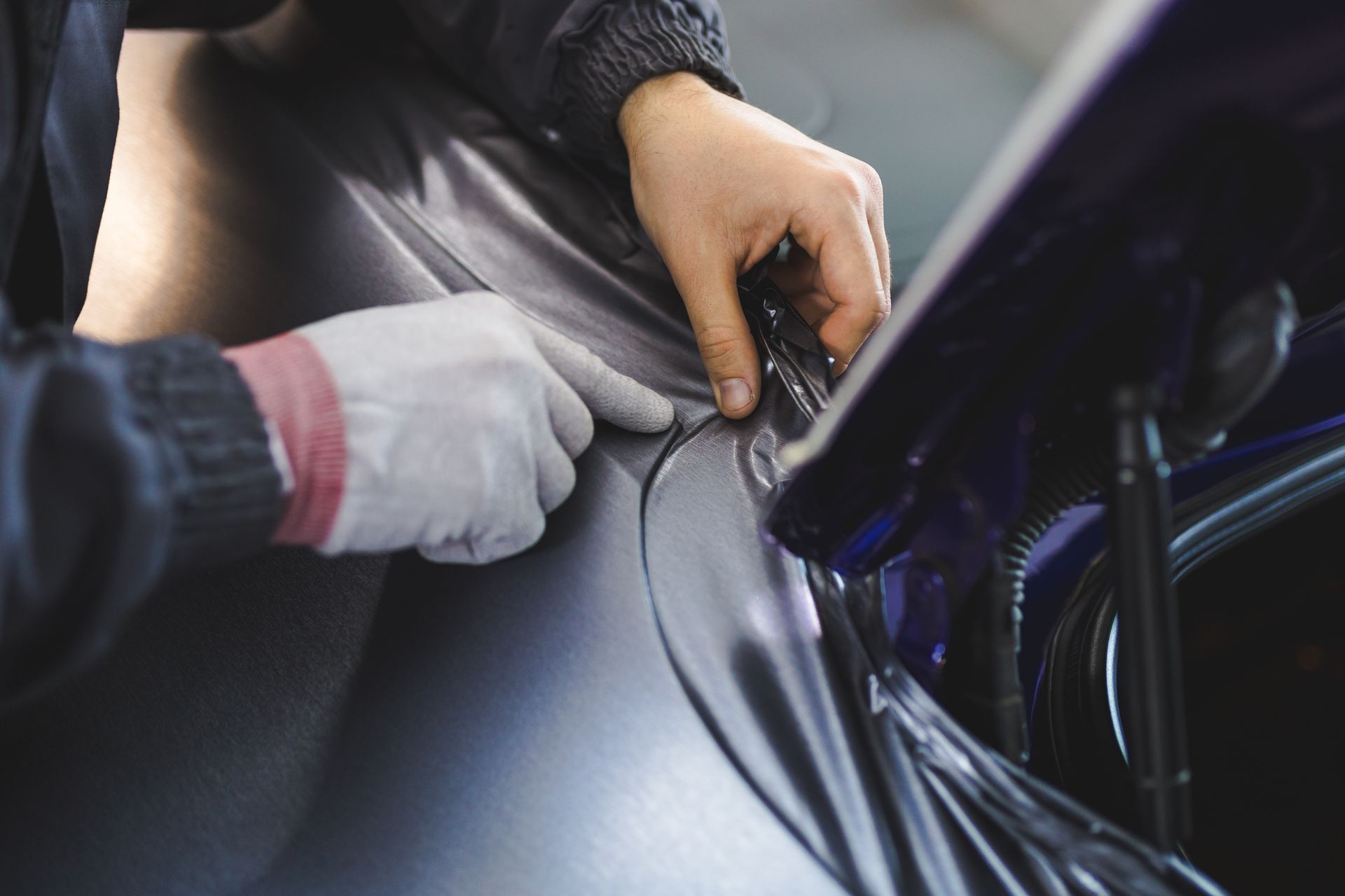 Une personne portant des gants noirs applique un revêtement sur la partie arrière d'une voiture grise, avec un feu arrière rouge vif.