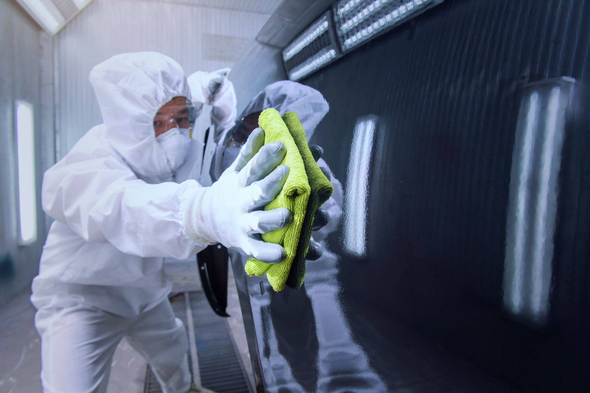 Une personne applique un film vinyle noir sur le capot d'une voiture à l'aide d'une raclette dans un garage.