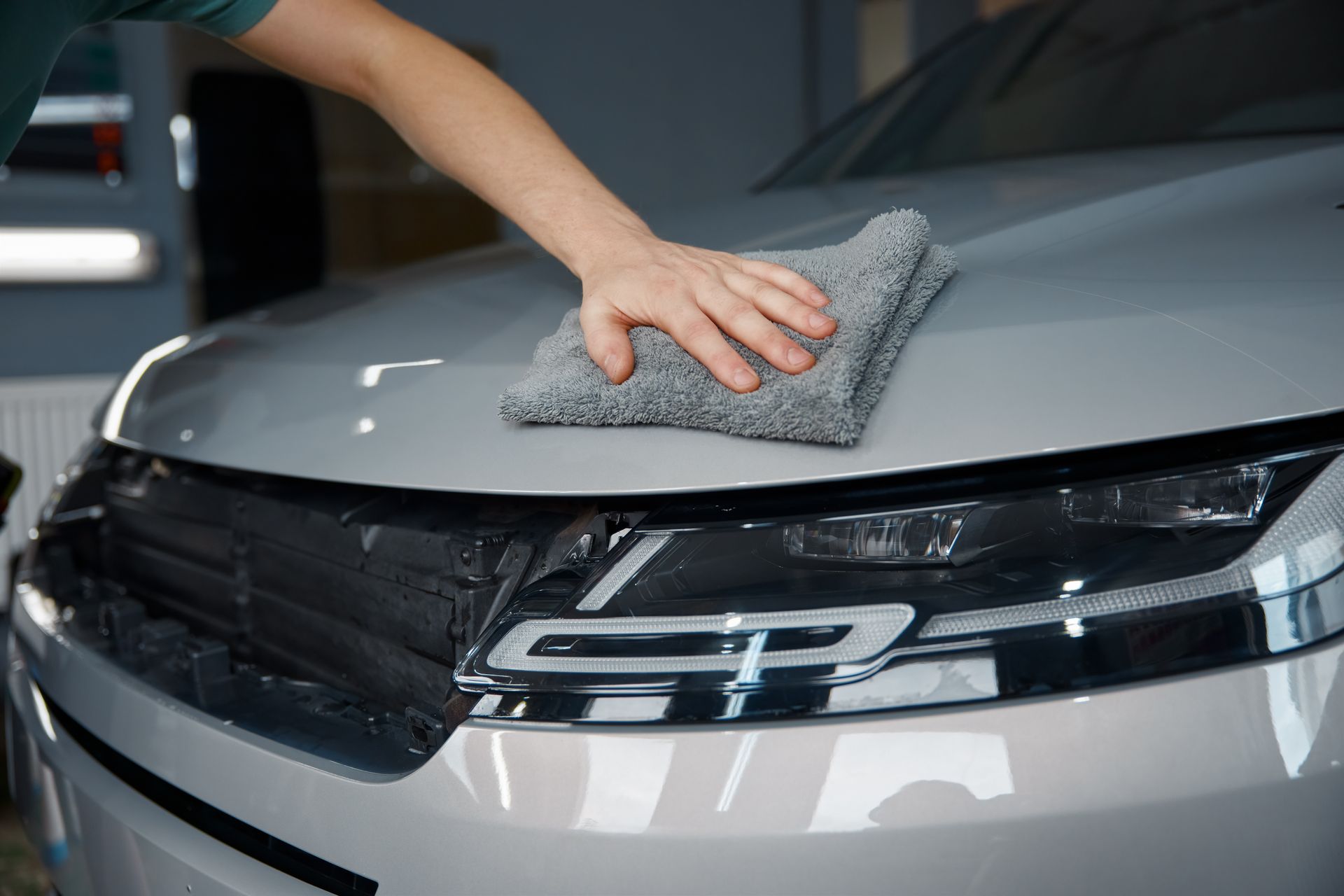 Voiture sur un pont élévateur dans un garage, autres voitures garées au sol, chariot à outils au premier plan.