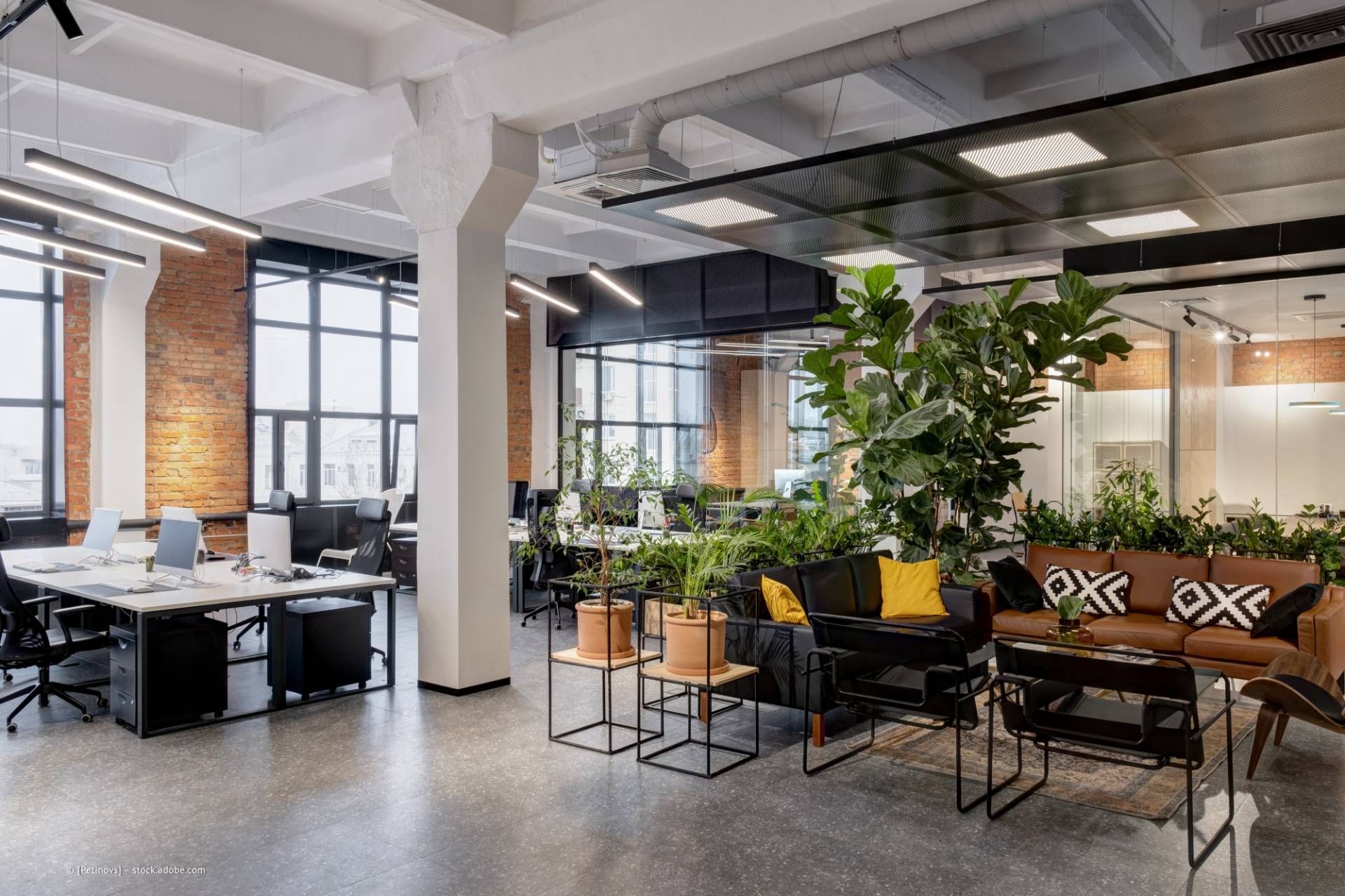 Großraumbüro mit Schreibtischen, Backsteinwänden, Zimmerpflanzen und einer Sitzecke.