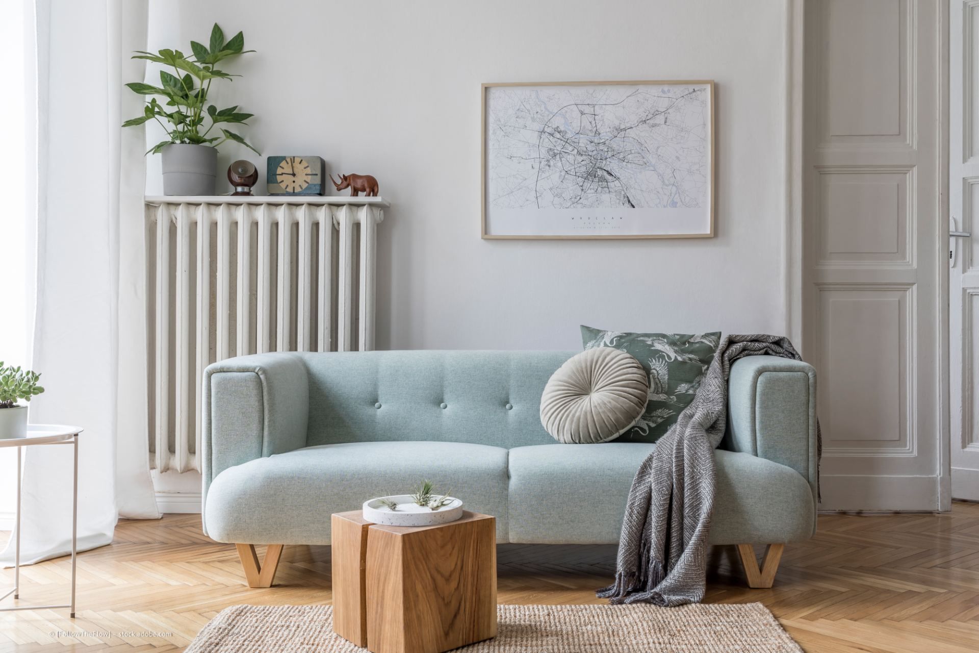 Hellblaues Sofa in einem hellen Zimmer mit Kunstwerken, einem Holztisch und einem Heizkörper.