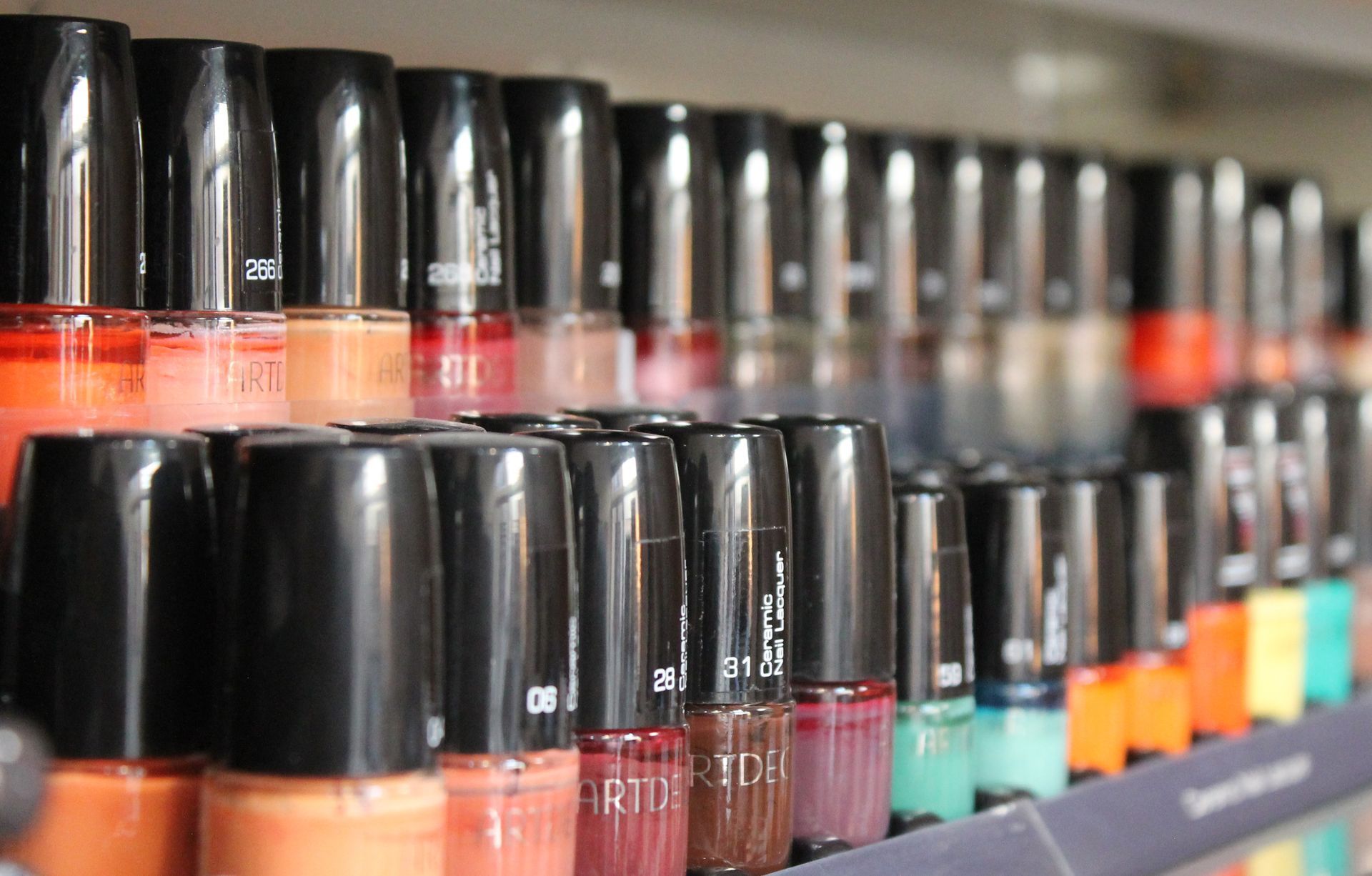 Filas de frascos de esmalte de uñas de colores con tapas negras en un estante.