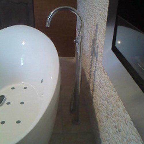 Baignoire ovale blanche, robinet argenté, mur texturé et meuble foncé dans une salle de bains.