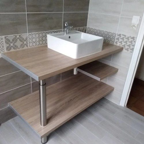 Salle de bains avec lavabo rectangulaire blanc sur un meuble-lavabo en bois à deux niveaux avec pieds argentés, contre un mur carrelé.