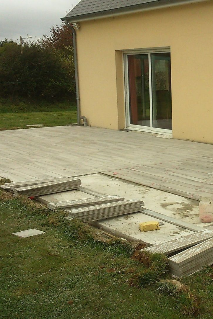 Terrasse en béton avec marches, jouxtant une maison jaune avec une porte-fenêtre coulissante et une pelouse verte.