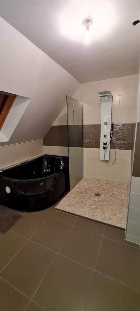 Une salle de bains avec une baignoire et une douche noires. La zone de douche est carrelée de carreaux imitation pierre.