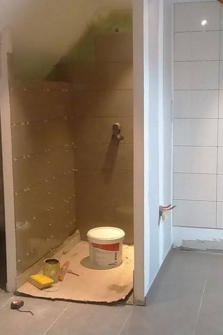 Salle de bains en construction, cabine de douche avec des murs partiellement carrelés, un seau et des outils.