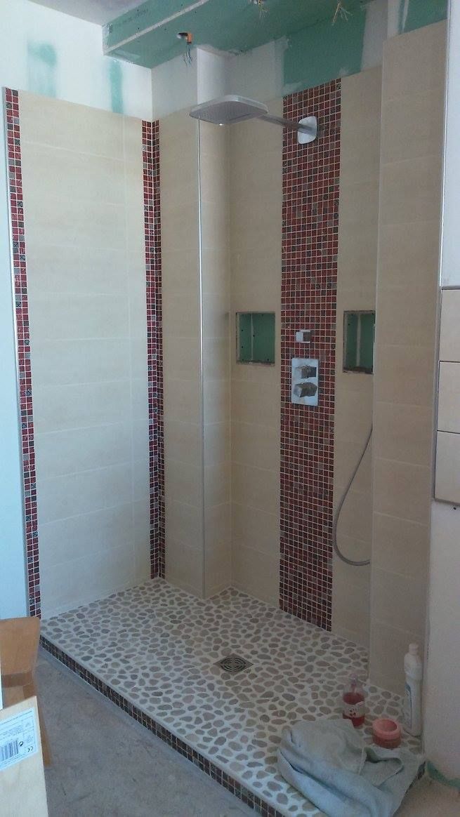 Cabine de douche en construction, accents de carrelage beige et rouge, sol en galets, robinetterie chromée.