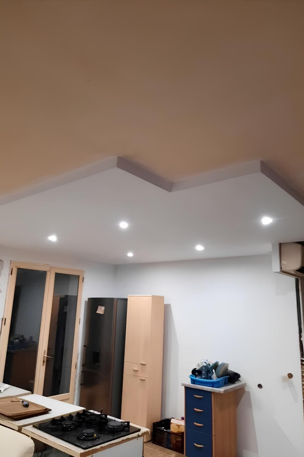 Cuisine avec plafond blanc, spots encastrés et placards. Une cuisinière à gaz est visible au premier plan.