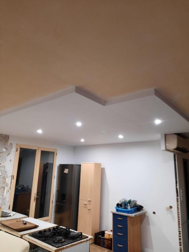 Cuisine avec plafond blanc orné de spots encastrés et d'une structure en gradins. Électroménagers et placards apparents.