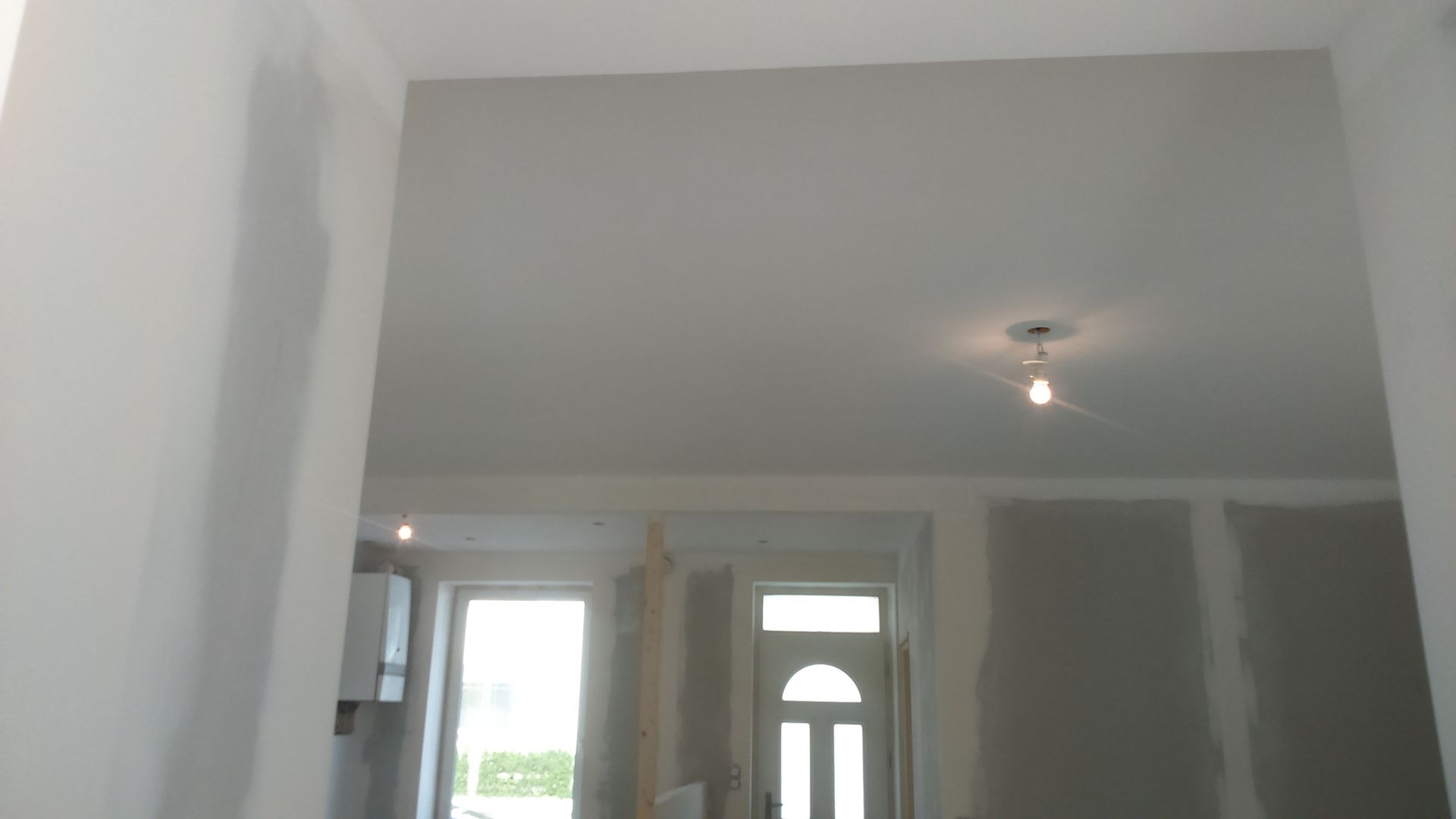 Vue intérieure d'une porte inachevée et d'une pièce avec des cloisons sèches et un luminaire au plafond.