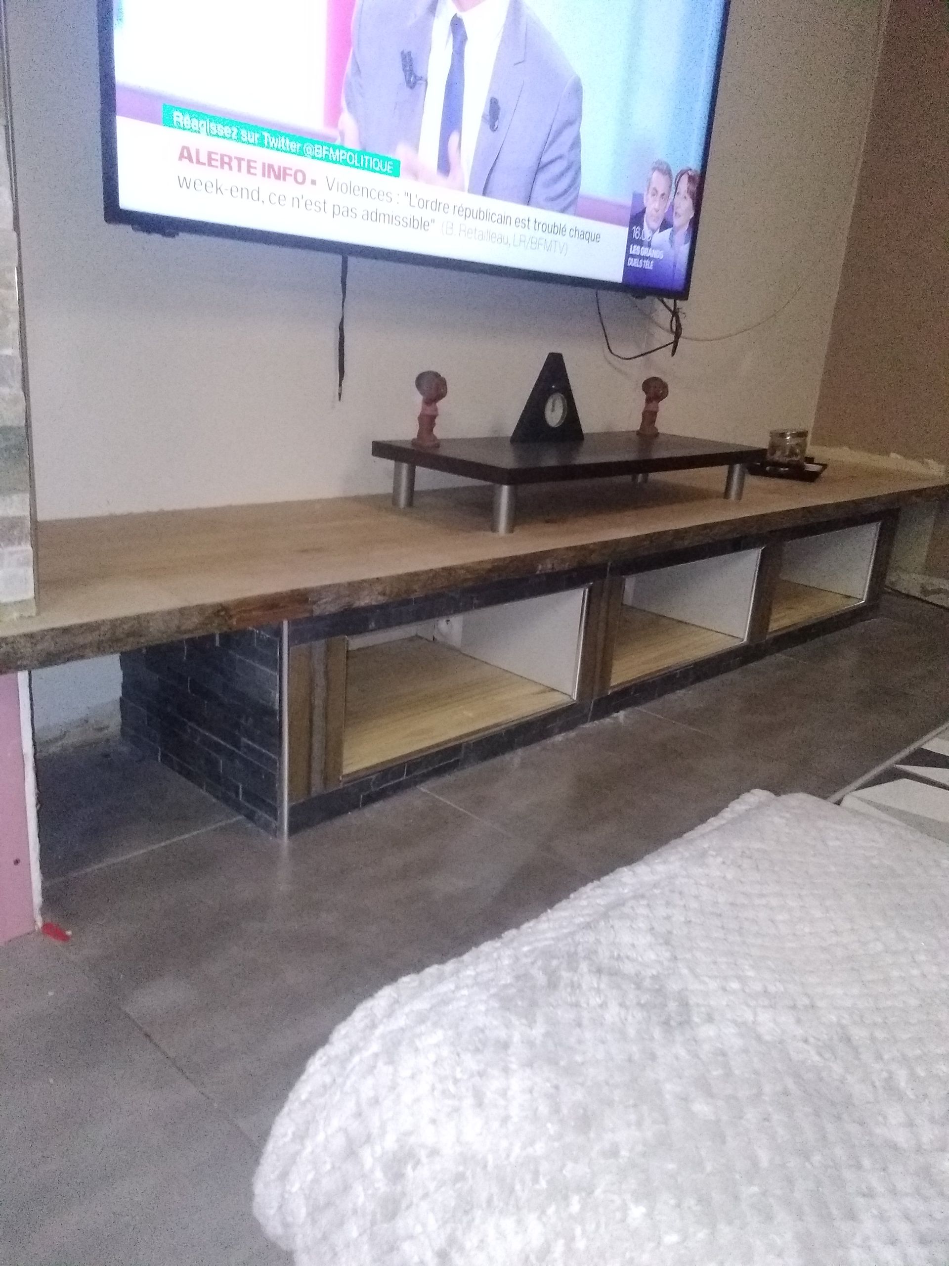 Téléviseur fixé au mur au-dessus d'un long meuble TV bas en bois avec des étagères ouvertes et une étagère surélevée au-dessus.