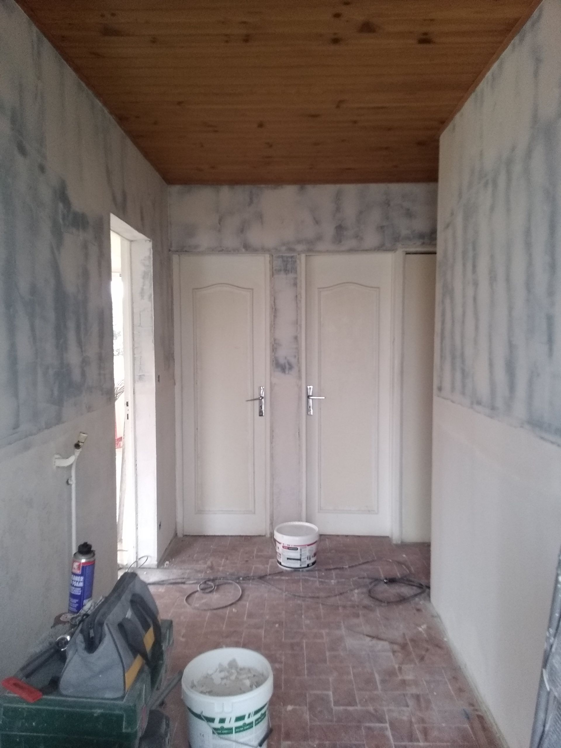 Couloir intérieur en cours de rénovation, avec portes, murs non finis et plafond en bois.