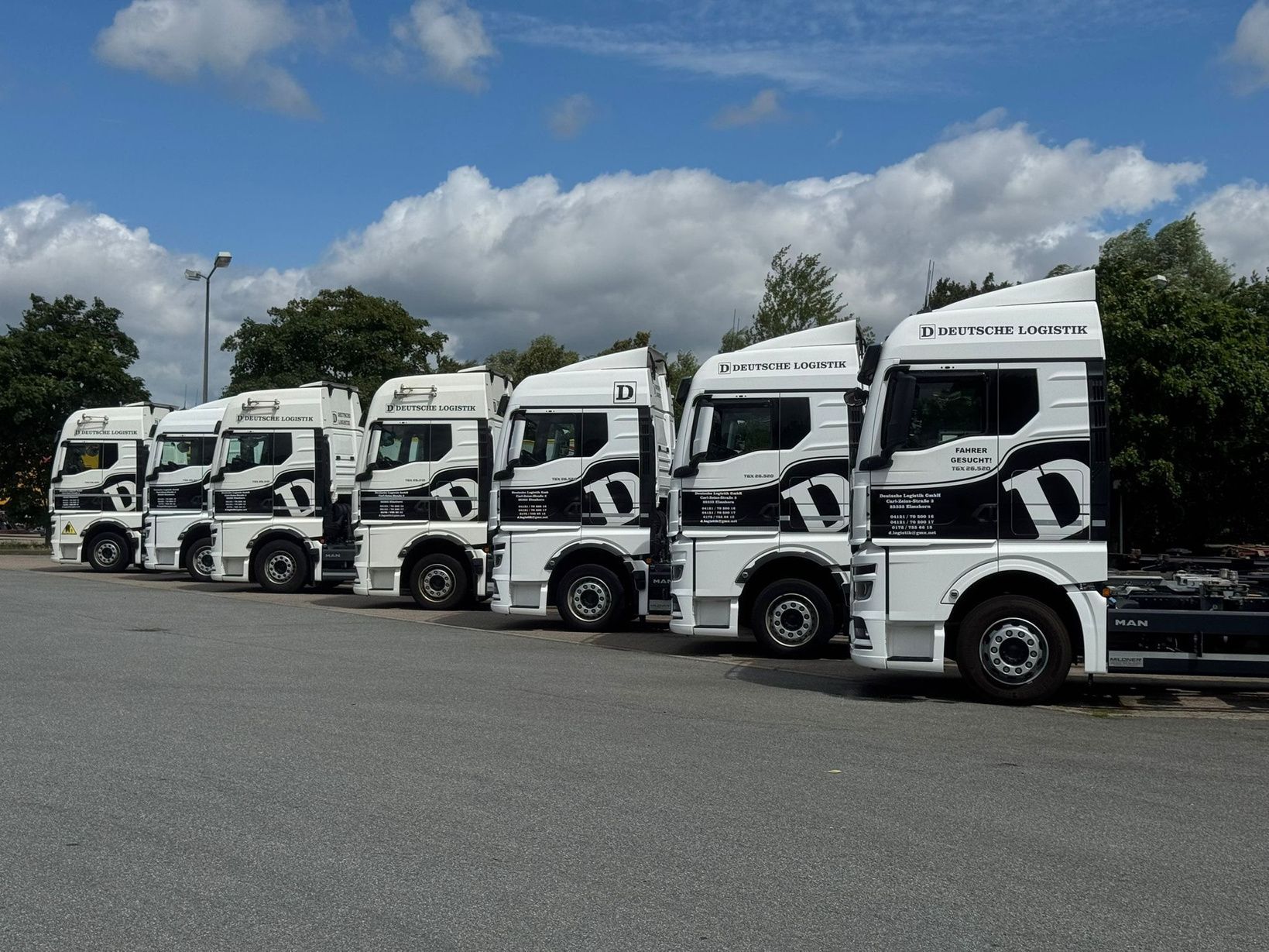 Weiße Lastwagen mit schwarzen Mustern parken an einem sonnigen Tag auf einem Parkplatz.