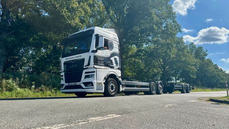 Eine Reihe weißer Lastwagen mit schwarzen Akzenten parkt auf dem Bürgersteig unter blauem Himmel.