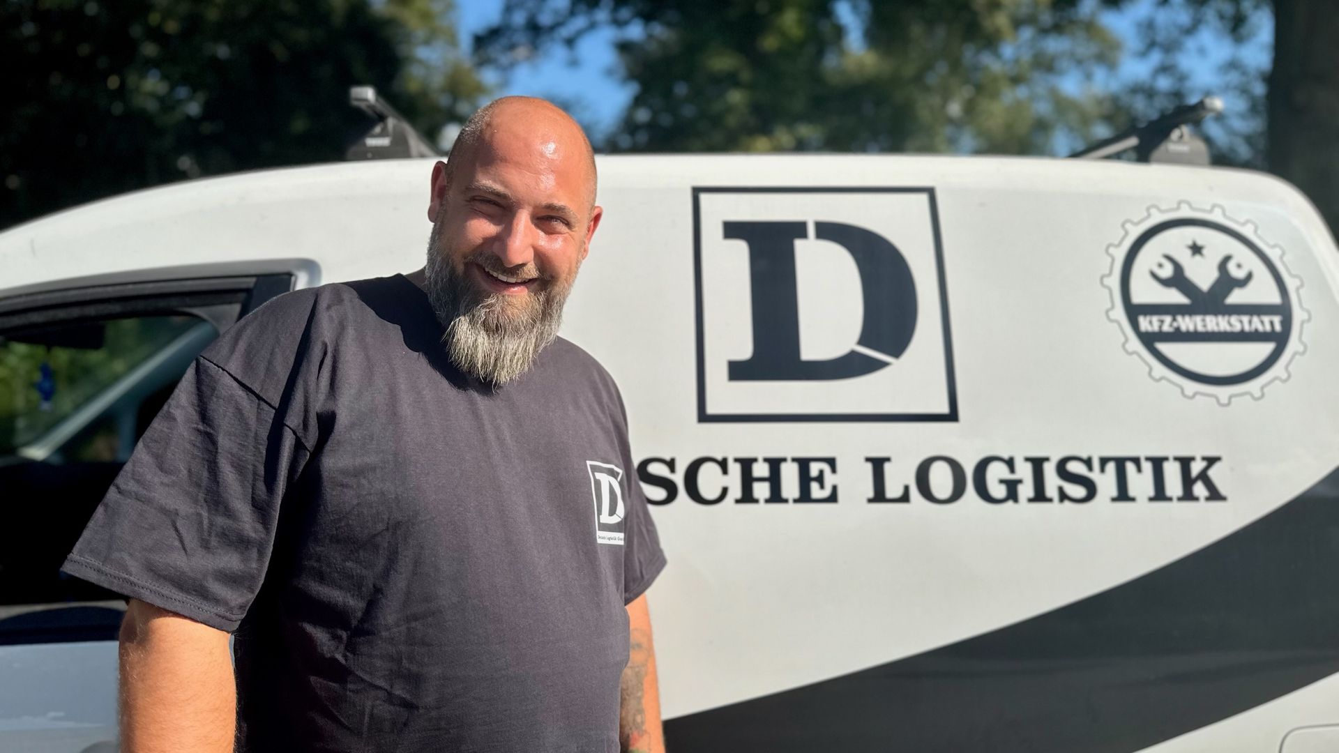 Lächelnder LKW-Fahrer in kariertem Hemd und Mütze, der im LKW telefoniert.