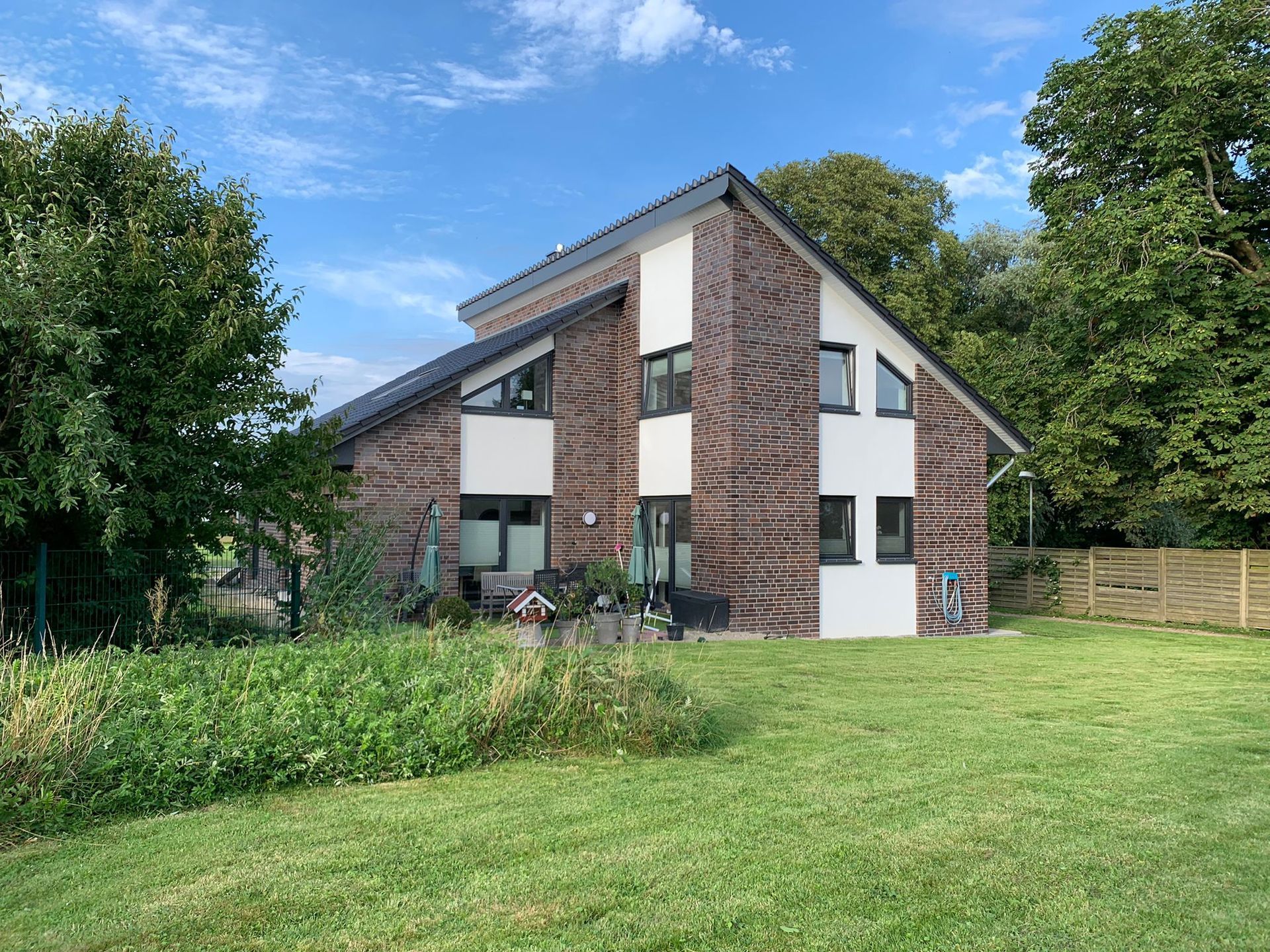 Ein großes Backsteinhaus mit vielen Fenstern steht inmitten einer üppigen grünen Wiese.