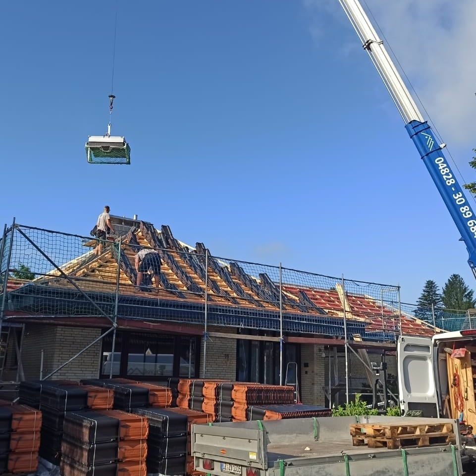 Ein Kran hebt ein Stück Dachmaterial über ein im Bau befindliches Gebäude.
