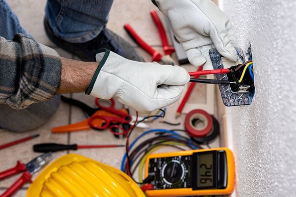 Un hombre está trabajando en una toma de corriente eléctrica con un multímetro.