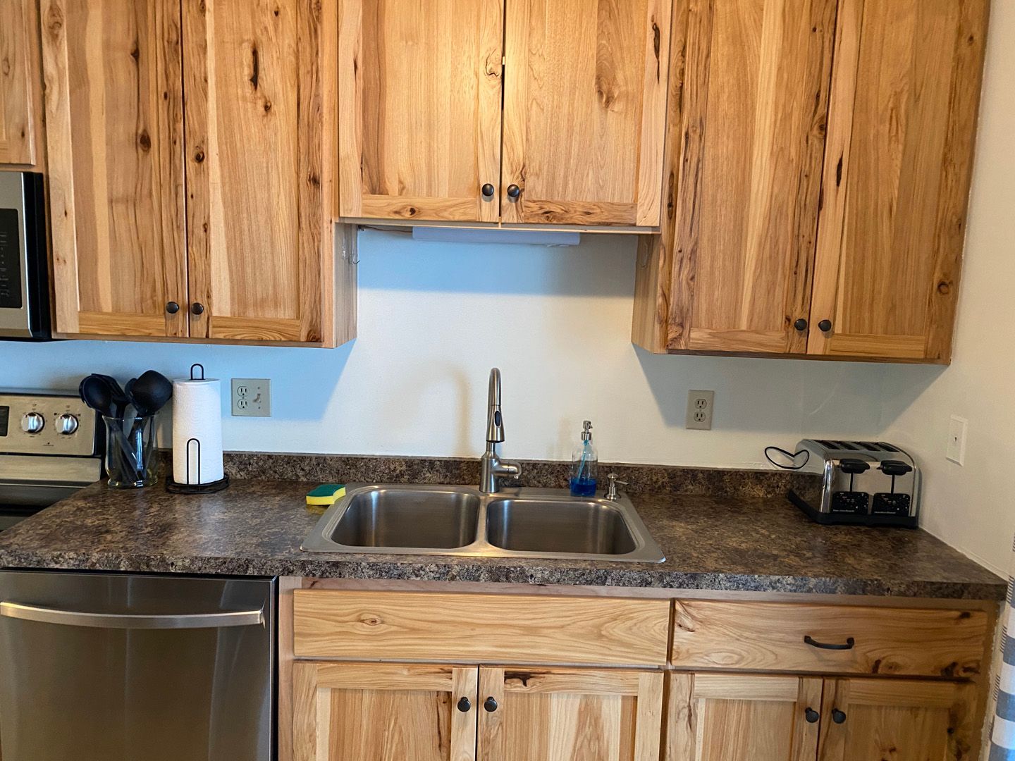 A kitchen with wooden cabinets , stainless steel appliances , a sink , and a toaster oven.