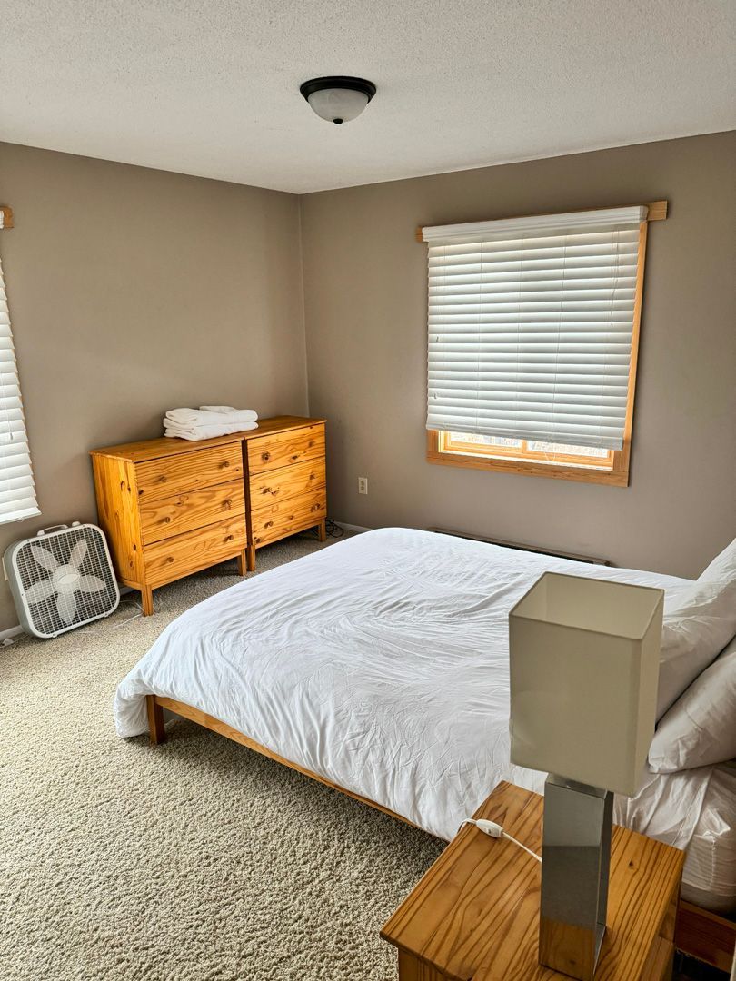 A bedroom with a bed , dresser , lamp and fan.