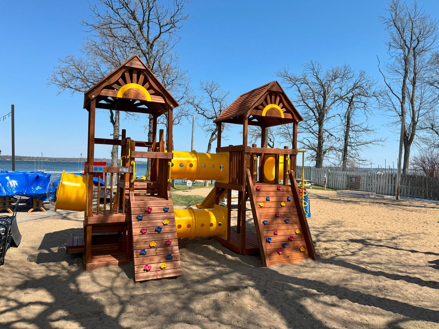 A wooden playground with a yellow slide and a climbing wall.
