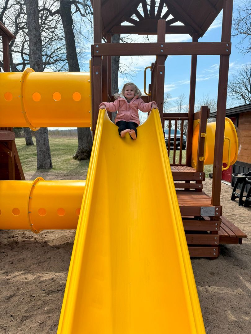 A little girl is sitting on a yellow slide at a playground.