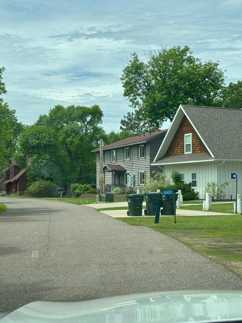 A white car is parked on the side of the road in front of a row of houses.