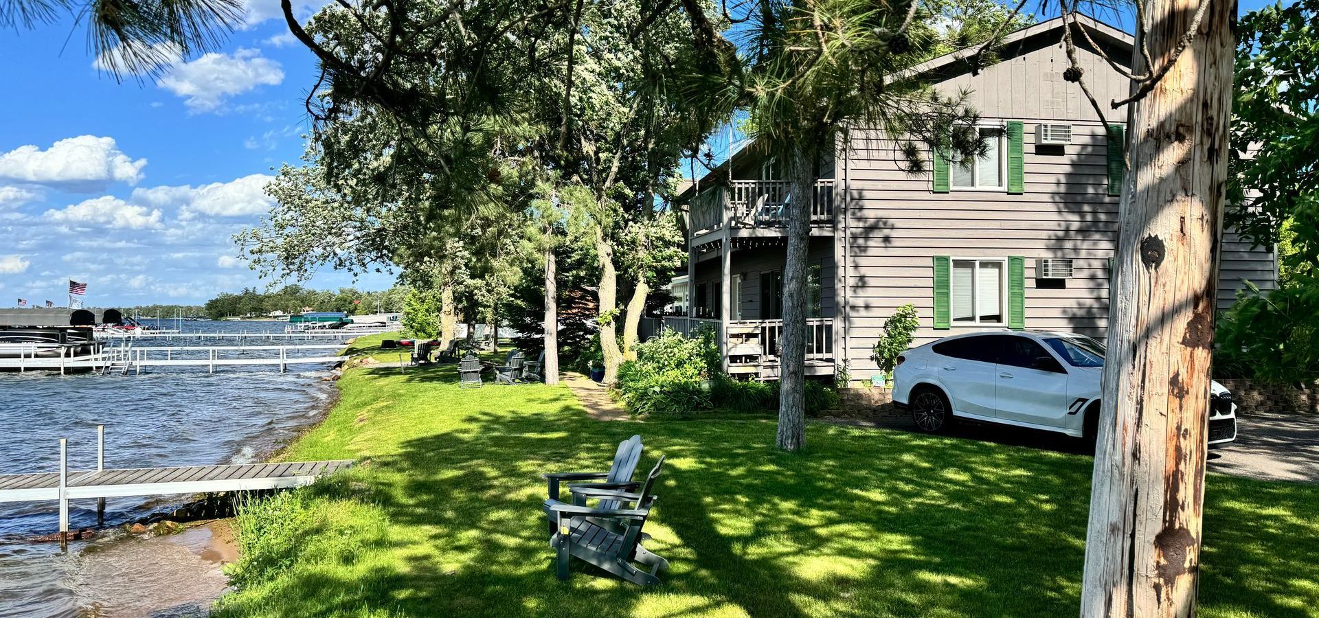 A white car is parked in front of a house next to a lake.
