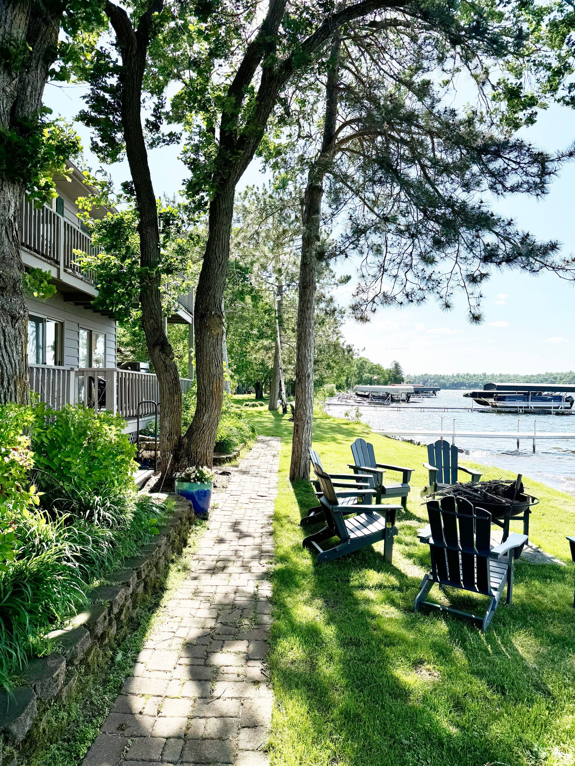 A brick walkway leading to a lake with chairs and a table.