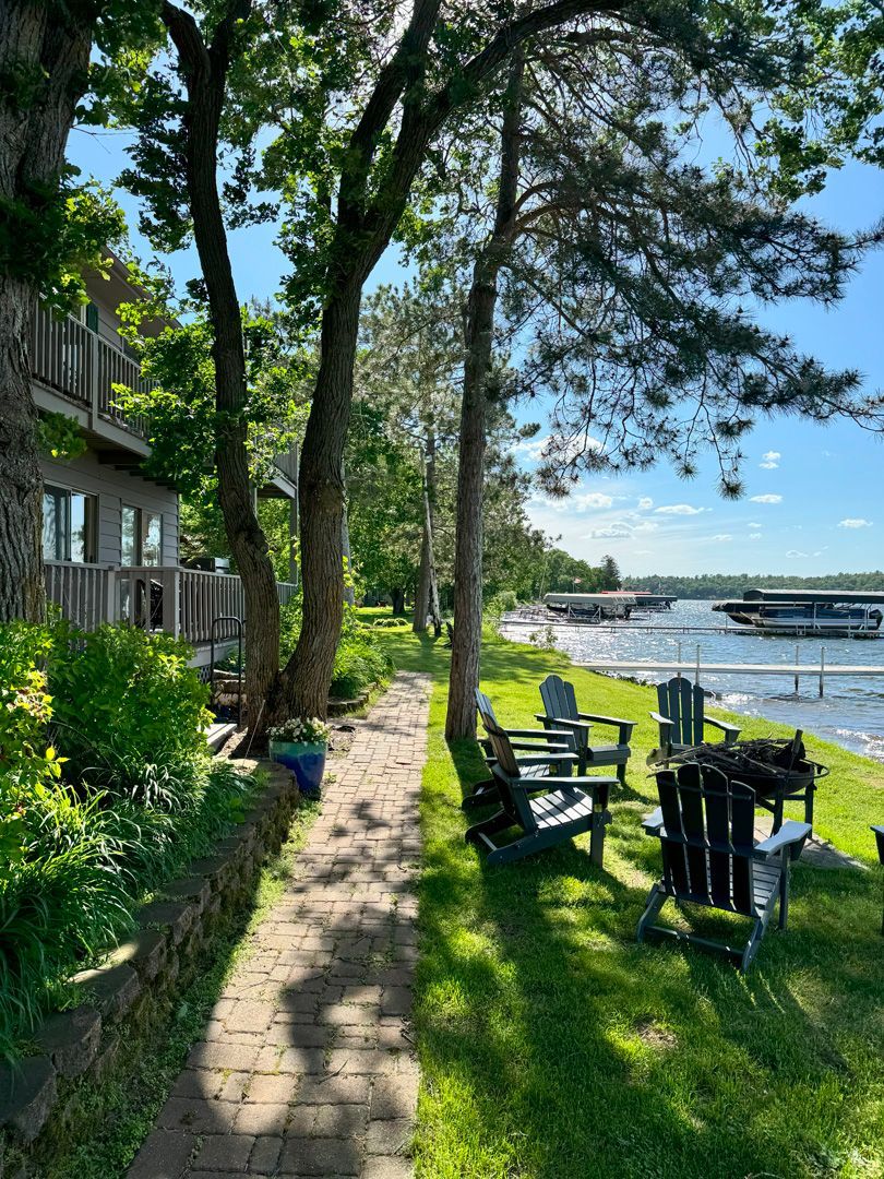 A brick walkway leading to a lake with chairs and trees.