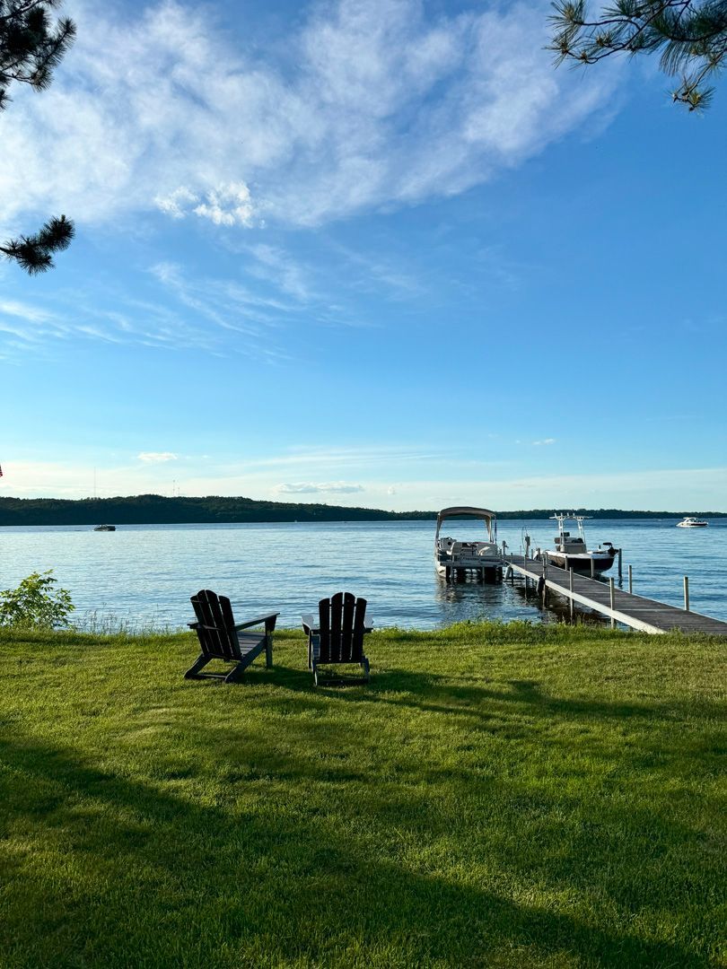 A couple of chairs sitting on top of a lush green field next to a body of water.