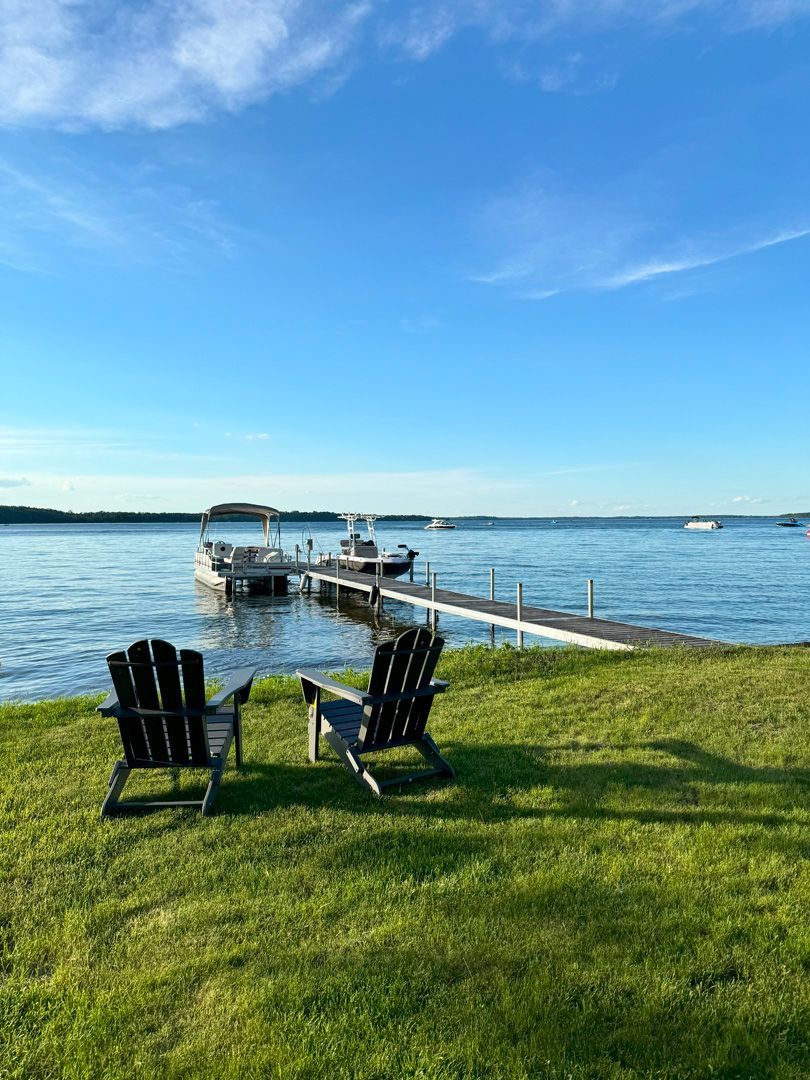A couple of chairs sitting on top of a lush green field next to a body of water.
