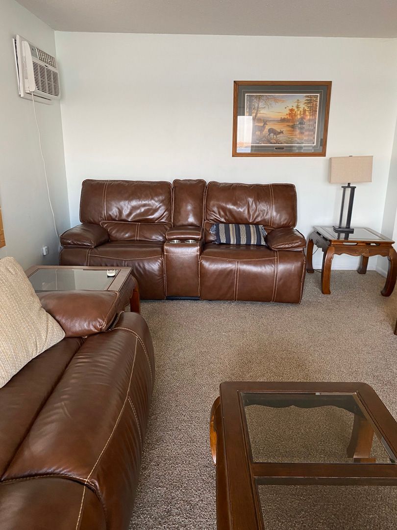 A living room with a brown leather couch and a glass coffee table.
