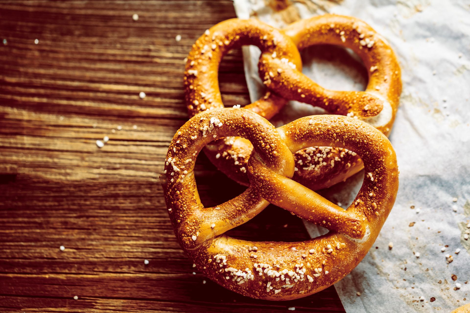 Deux bretzels dorés, saupoudrés de gros sel, reposent sur une surface en bois et du papier sulfurisé.