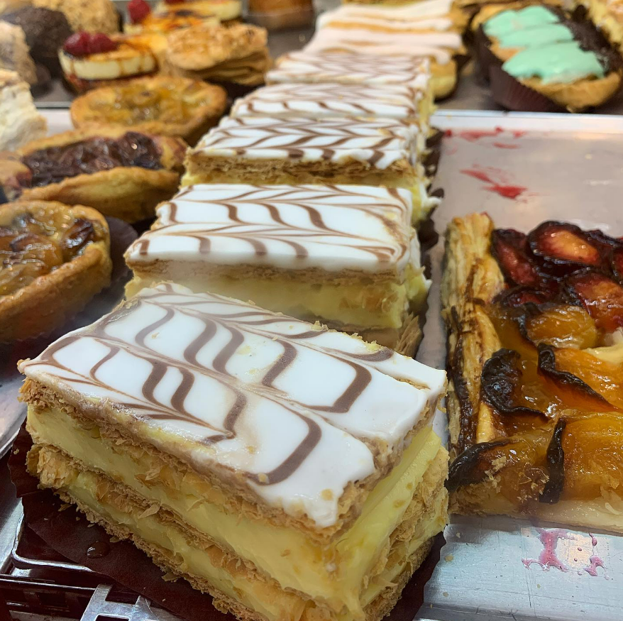 Présentation de pâtisseries dans une vitrine de boulangerie, notamment un mille-feuille à plusieurs couches avec glaçage et des tartelettes aux fruits.