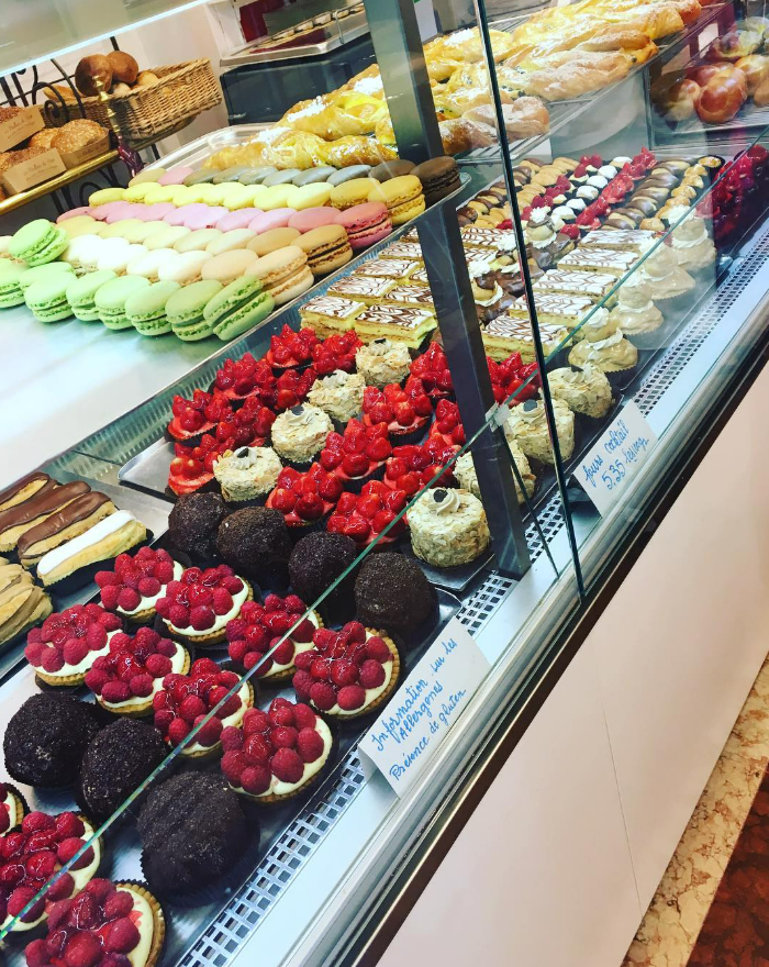 Pâtisseries en vitrine : macarons colorés, tartelettes aux framboises, autres desserts.