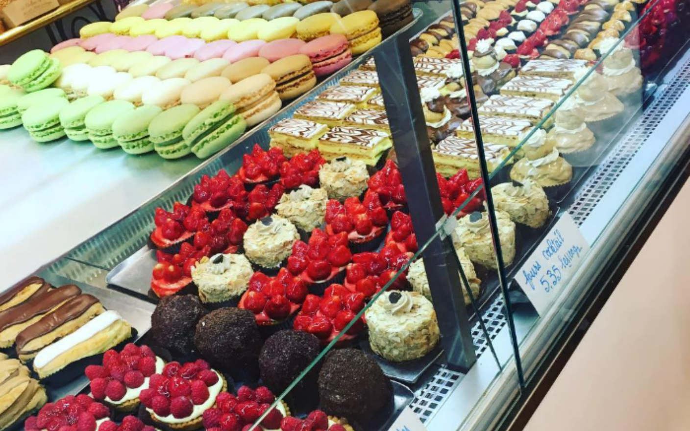 Pâtisseries dans une vitrine : macarons, tartelettes aux fruits rouges et autres desserts.