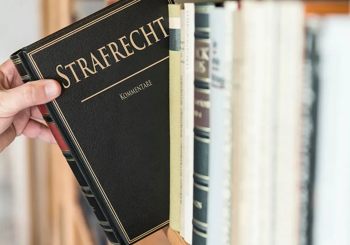 Ein Rechtsanwalt für Strafrecht aus Bonn hält ein Buch mit dem Titel „Strafrecht“ vor einem Bücherregal.