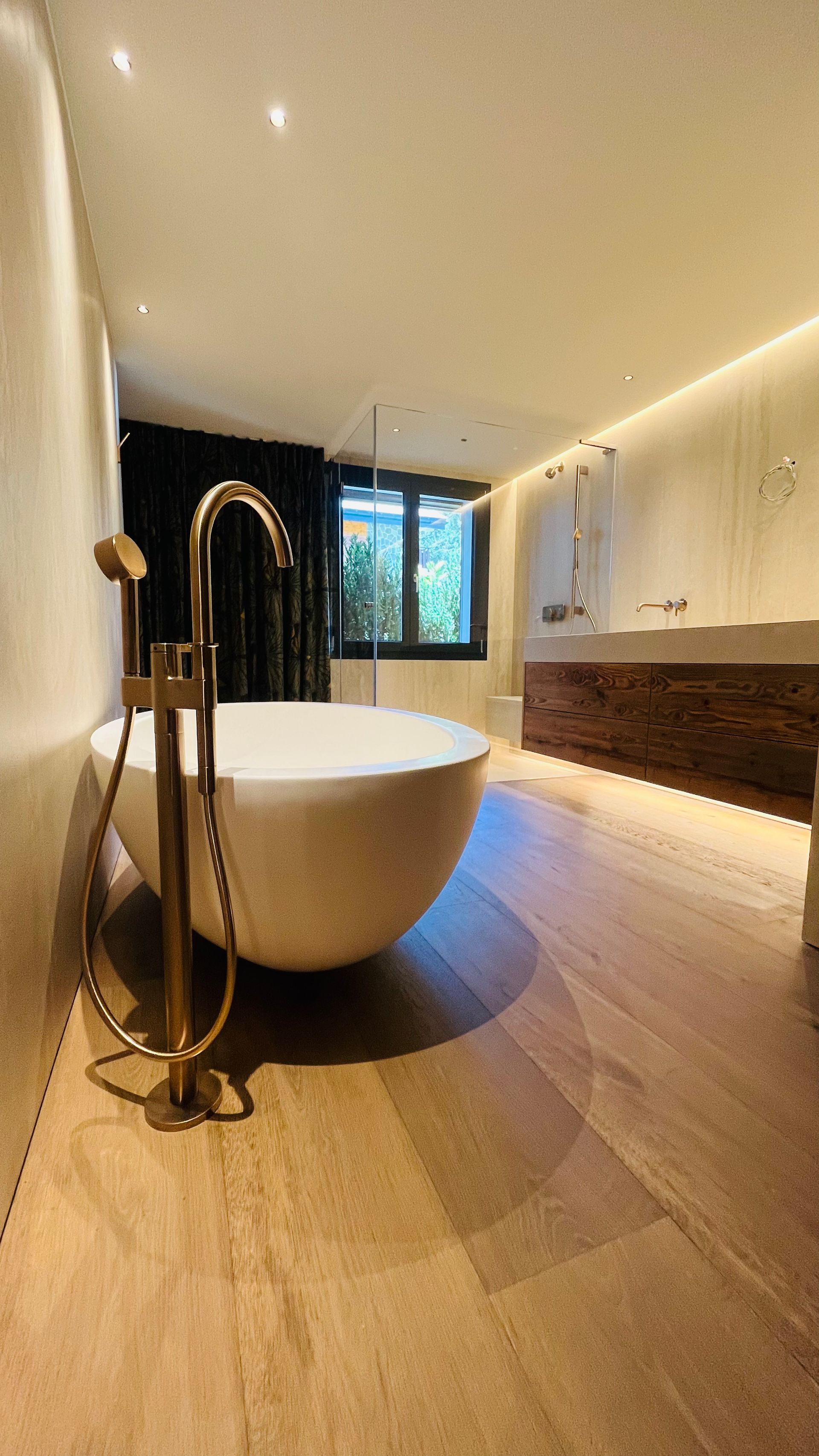 De l'eau se déverse d'une baignoire blanche sur un tapis clair dans une pièce avec une fenêtre, un banc et des rideaux.