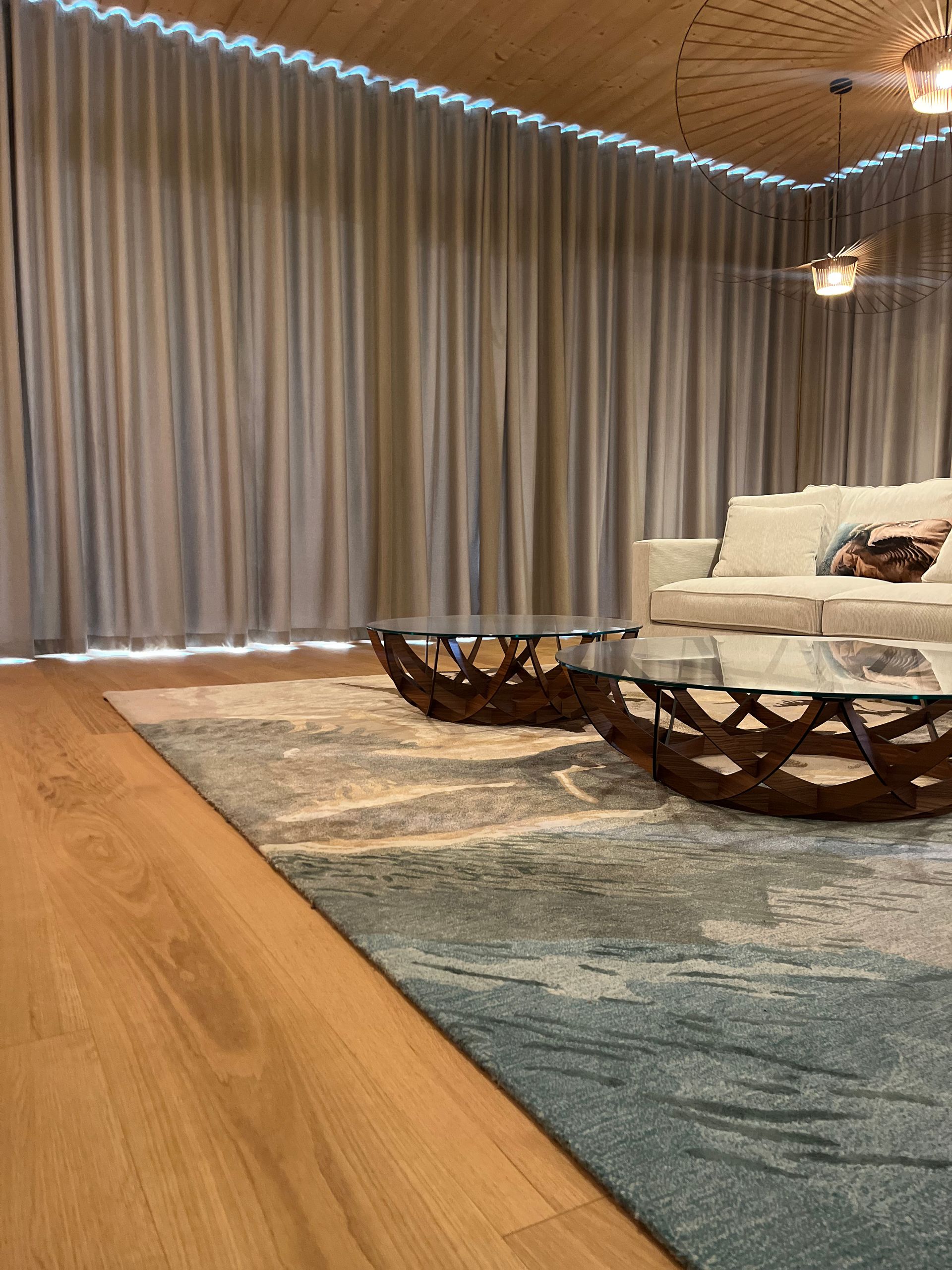 Salon cosy avec moquette à carreaux, murs en bois, canapé marron avec coussins décoratifs et tapisserie représentant une forêt.