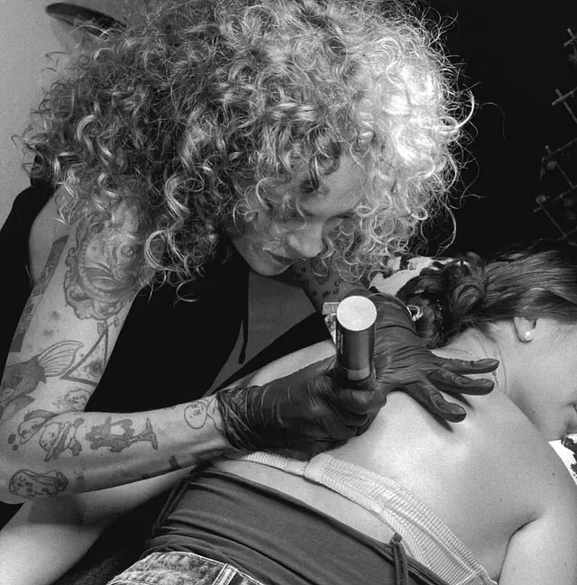 Una mujer con cabello rizado se está haciendo un tatuaje en la espalda de otra mujer.