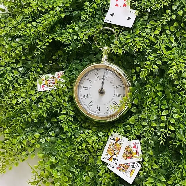 Un reloj de bolsillo está sobre una planta verde rodeado de naipes.