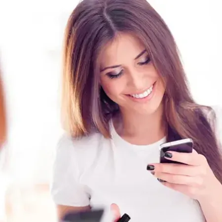 Una mujer sonríe mientras mira su teléfono celular.