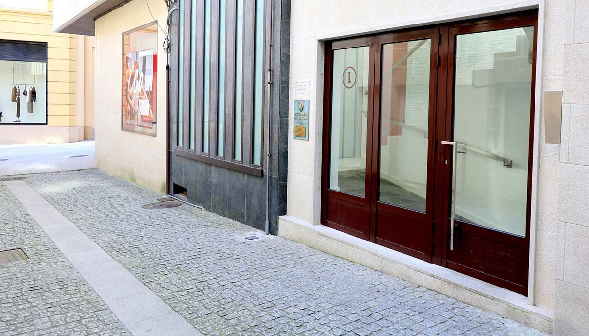 Callejón adoquinado con puerta de cristal y portón metálico. Póster en la pared.