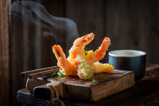 Crevettes tempura sur une planche en bois avec baguettes et sauce, vapeur s'échappant.
