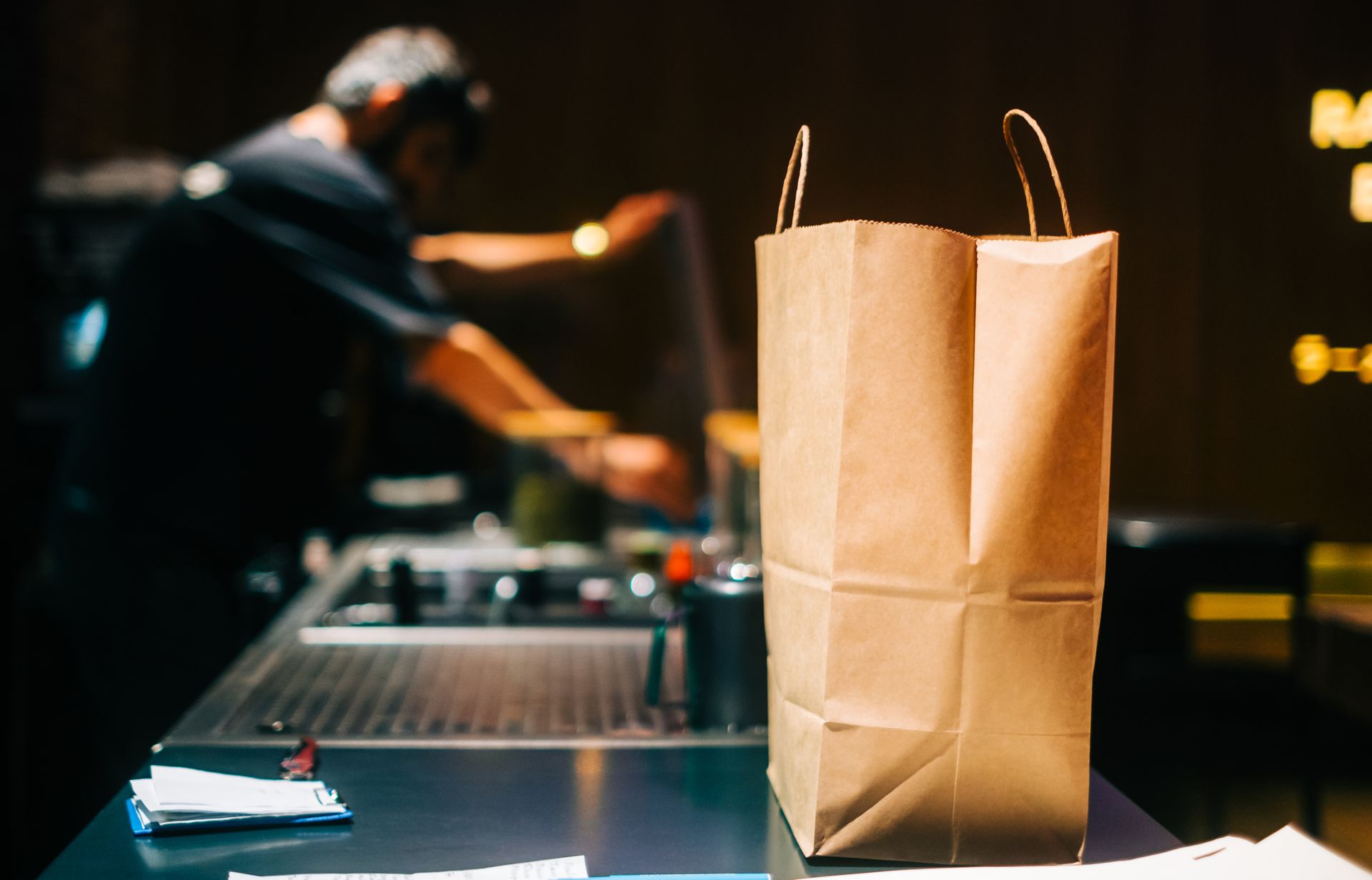 Sac en papier brun à emporter sur un comptoir, employé de restaurant en arrière-plan.