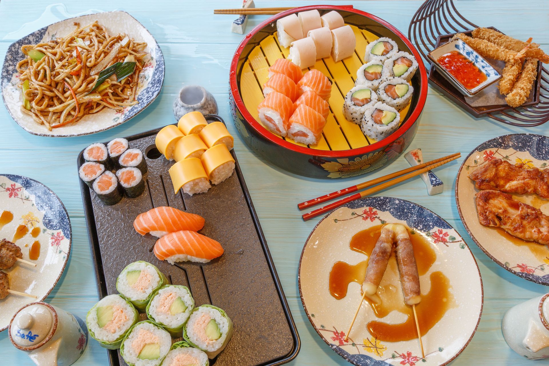 Assortiment de sushis, nouilles et autres plats asiatiques disposés sur une table.