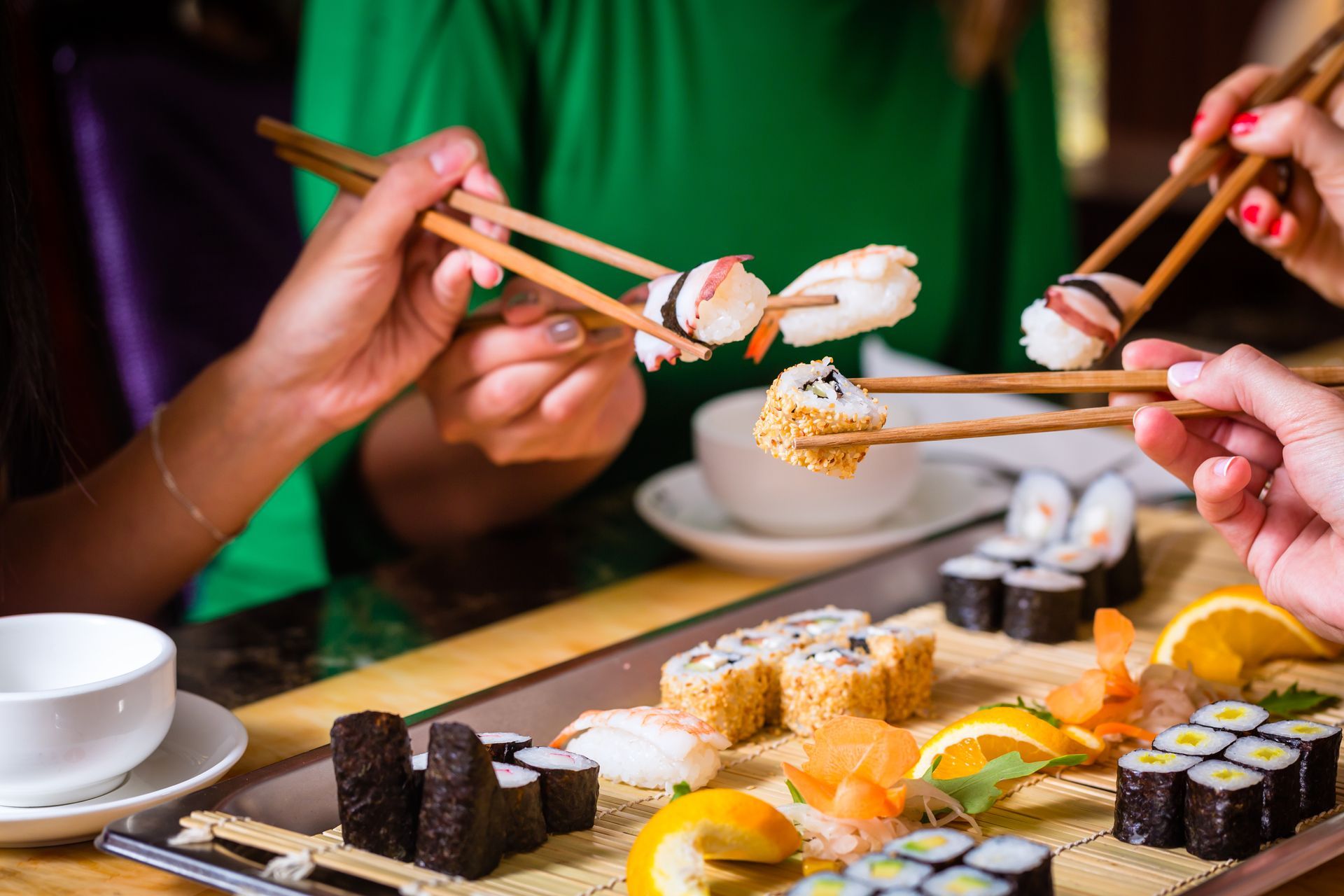 Des personnes mangent des sushis avec des baguettes à une table ; on aperçoit différents types de rouleaux.