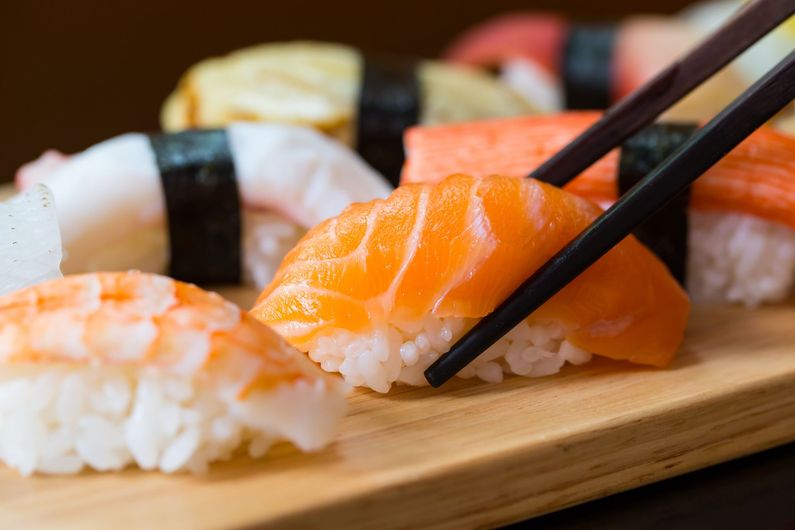 Sushi nigiri sur une planche en bois ; baguettes attrapent un morceau de saumon.